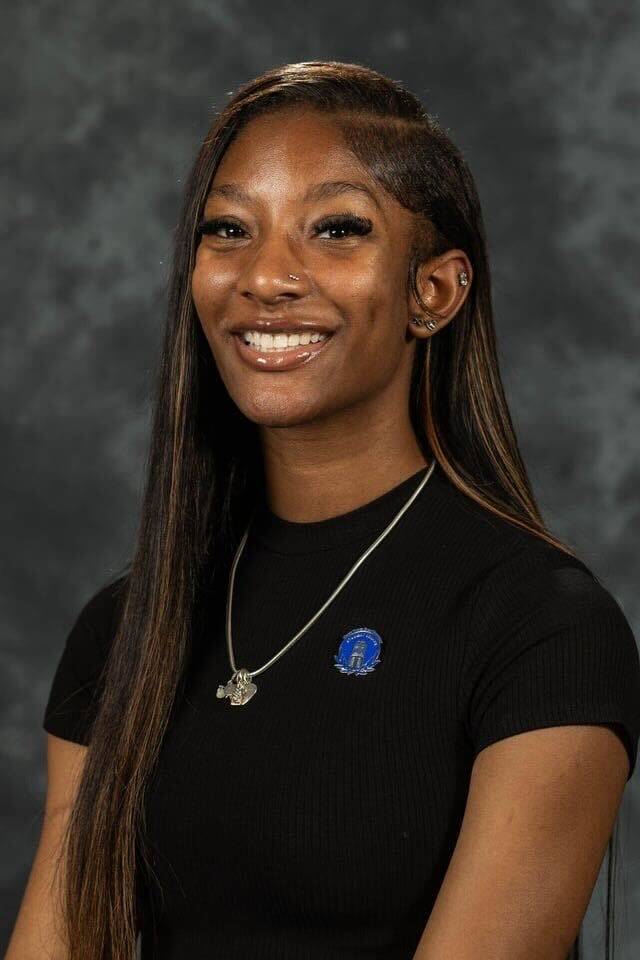 Image 1 of 2 Person smiling in black shirt against gray background.